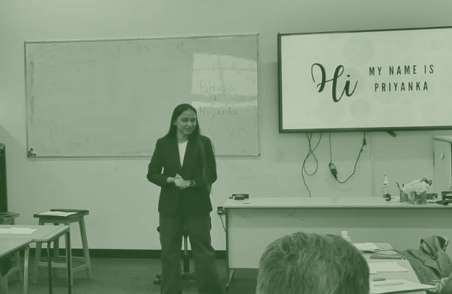 Priyanka presenting to a room, standing beside a screen that reads Hi, my name is Priyanka